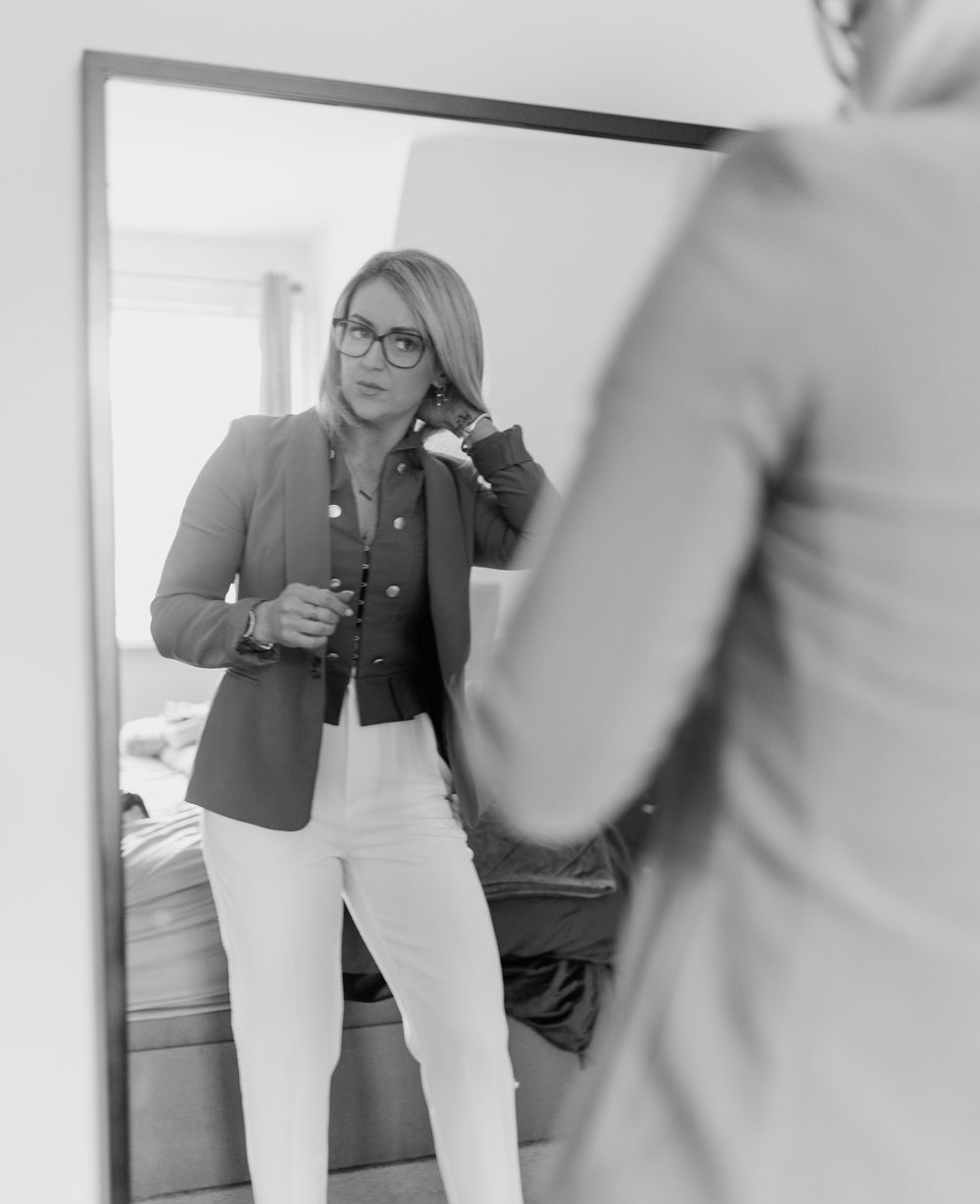 Black and white photo of Maria Morgan looking at herself in a full-length mirror