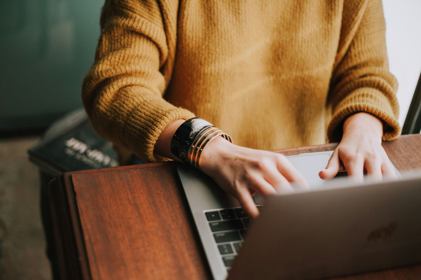 Hands typing on a laptop, in a mustard jumper